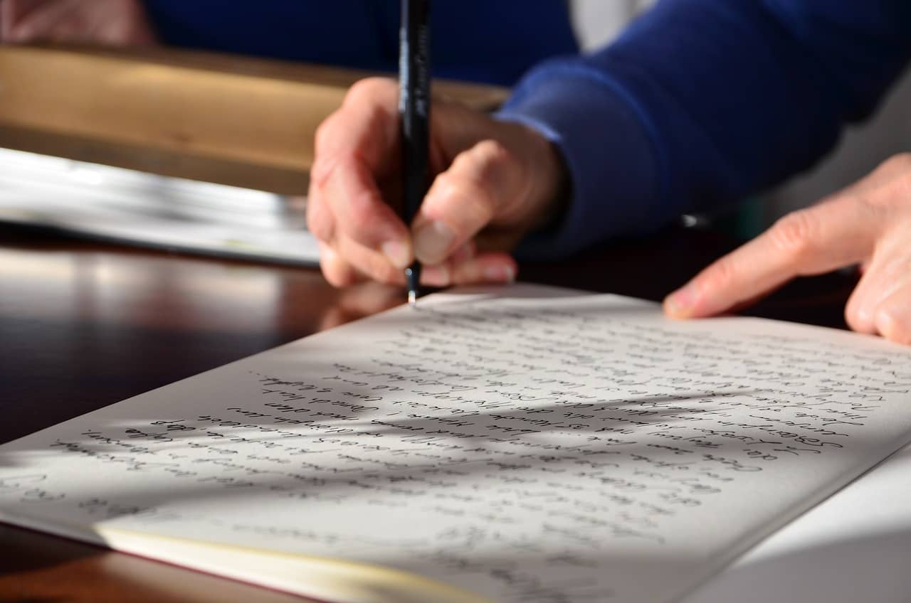 Close-up of a person's hands writing an essay with a black pen on a paper, symbolizing custom essay writing services.