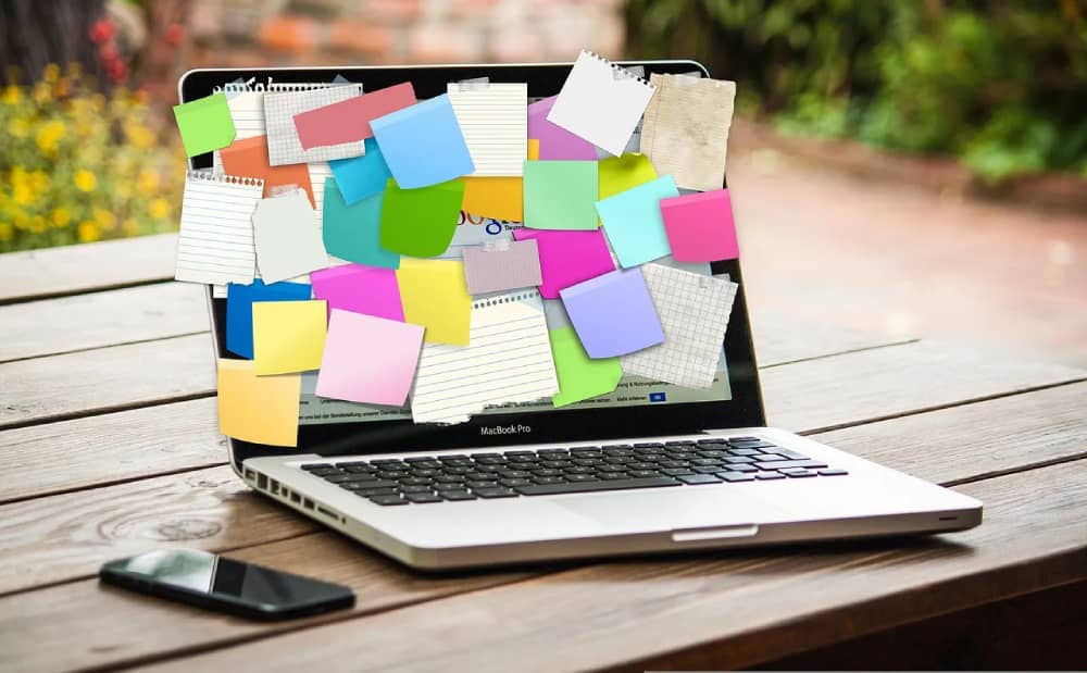 Laptop buried under colorful sticky notes and paper reminders symbolizing student stress.