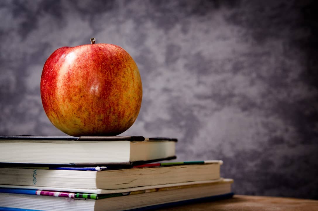 A ripe apple resting on a stack of textbooks against a textured grey background, symbolizing knowledge and learning.