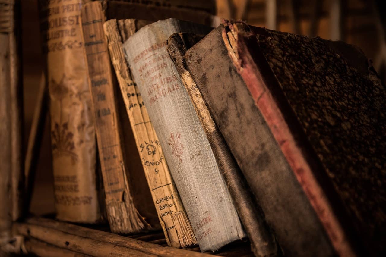 Antique books stacked on a shelf, showcasing their aged and worn covers.